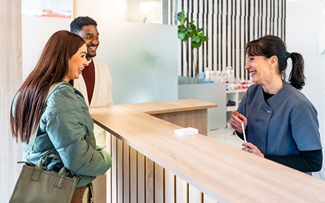 Dental receptionist smiling at couple in lobby