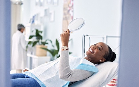 Woman smiling at reflection in handheld mirror