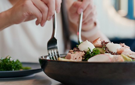 Hands using fork and knife to scoop salad onto their plate