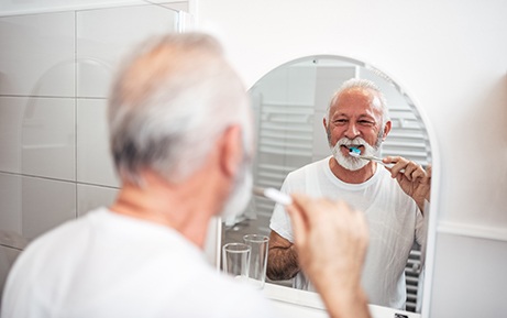 Man smiling while brushing his teeth in bathroom