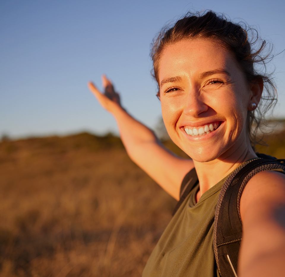 Woman smiling outside with arm outstretched