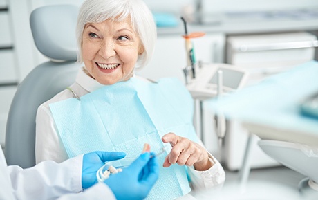Gloved hands handing dentures to woman in dental chair