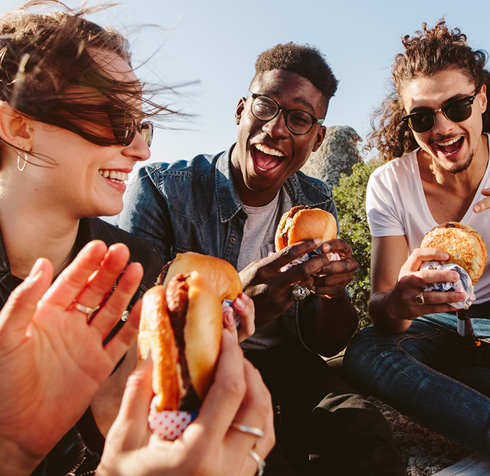 Group of adults eating burgers outdoors after replacing missing teeth in Clearwater