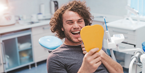 Young man looking at his smile in a mirror after receiving dental services in Clearwater