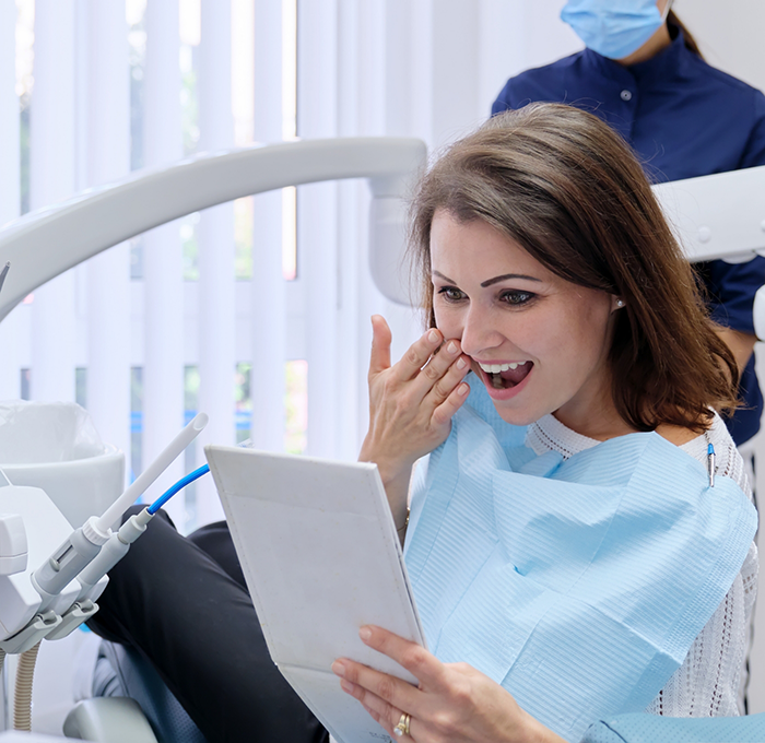 Woman admiring her smile in a mirror after restorative dentistry in Clearwater
